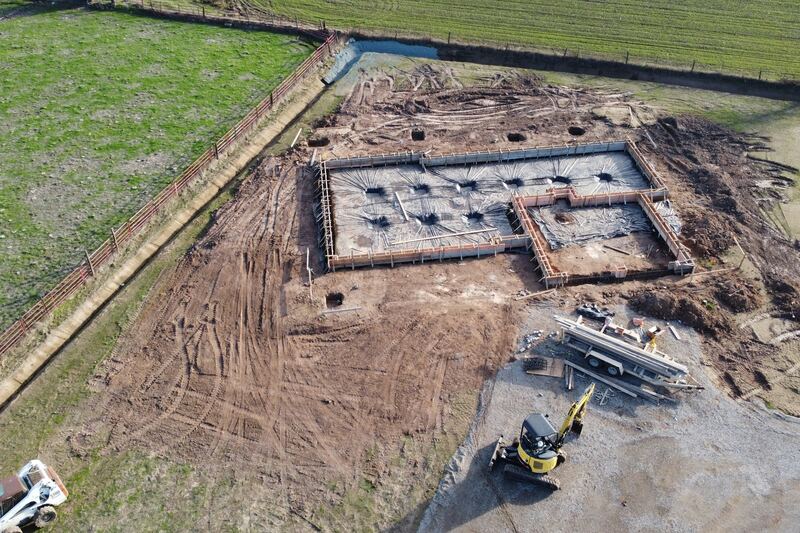 Vue aérienne d’un terrain en chantier : coffrages des fondations d’une maison et mini-pelle.