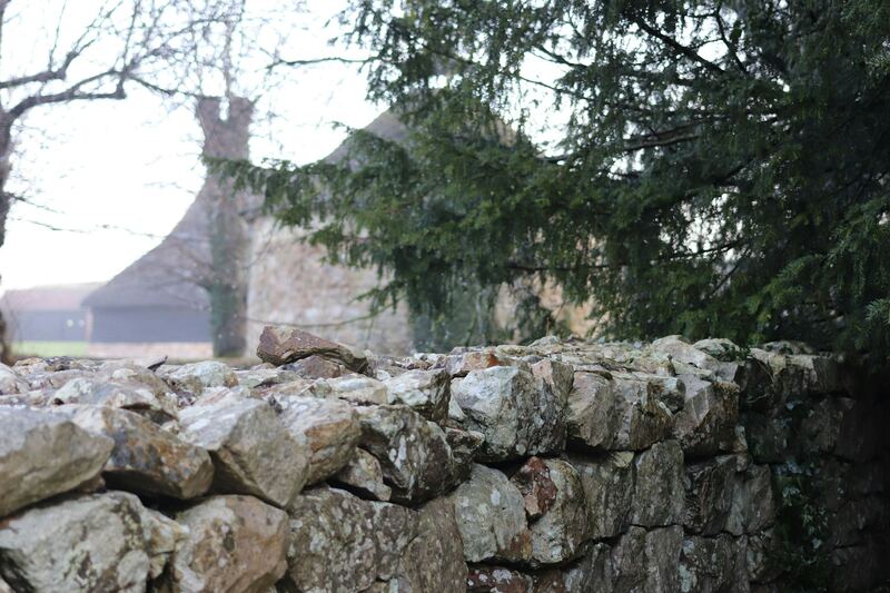 Mur de pierres sèches devant un bâtiment de ferme, en hiver.