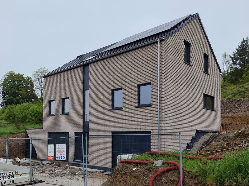 Maison neuve en briques beiges sur un chantier, avec le panneau et la remorque de Mathieu Schulzen Construction.