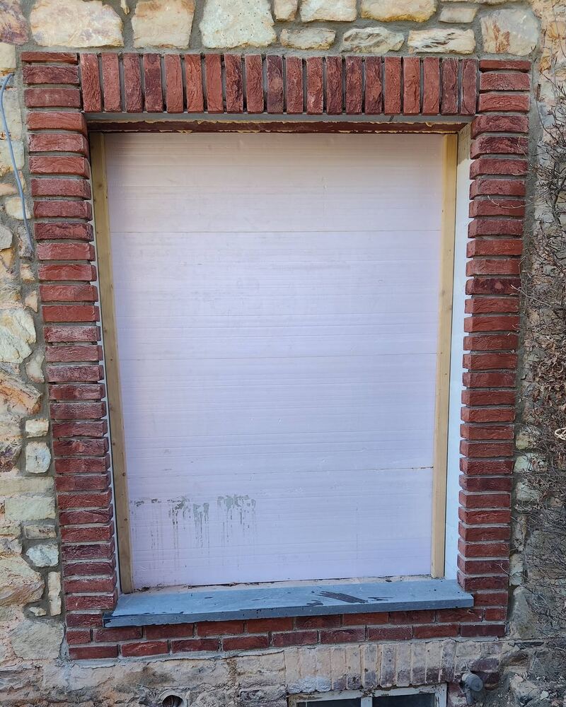 Encadrement de fenêtre en briques rouges dans un vieux mur en moellons, avec un seuil en pierre bleue.