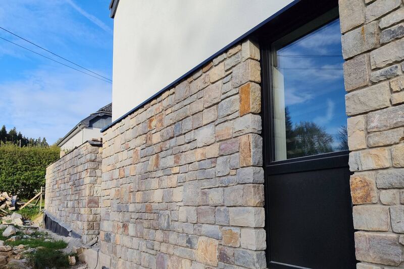 Parement en pierre naturelle au rez-de-chaussée d’une maison neuve, autour d’une baie anthracite.